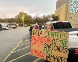 Data Centers invasion of the water snatchers and energy vampires on a sign held by a lady in the street